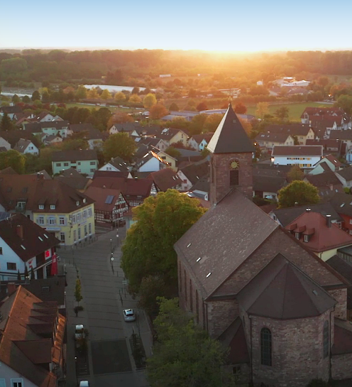 Luftaufnahme von Iffezheim bei Sonnenuntergang, die warmen Farben des Himmels spiegeln sich in den Gebäuden wider.